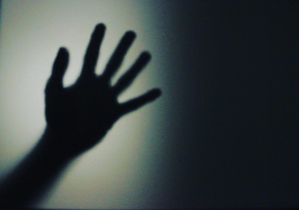 A shadowy silhouette of a hand in front of a softly lit dark background.