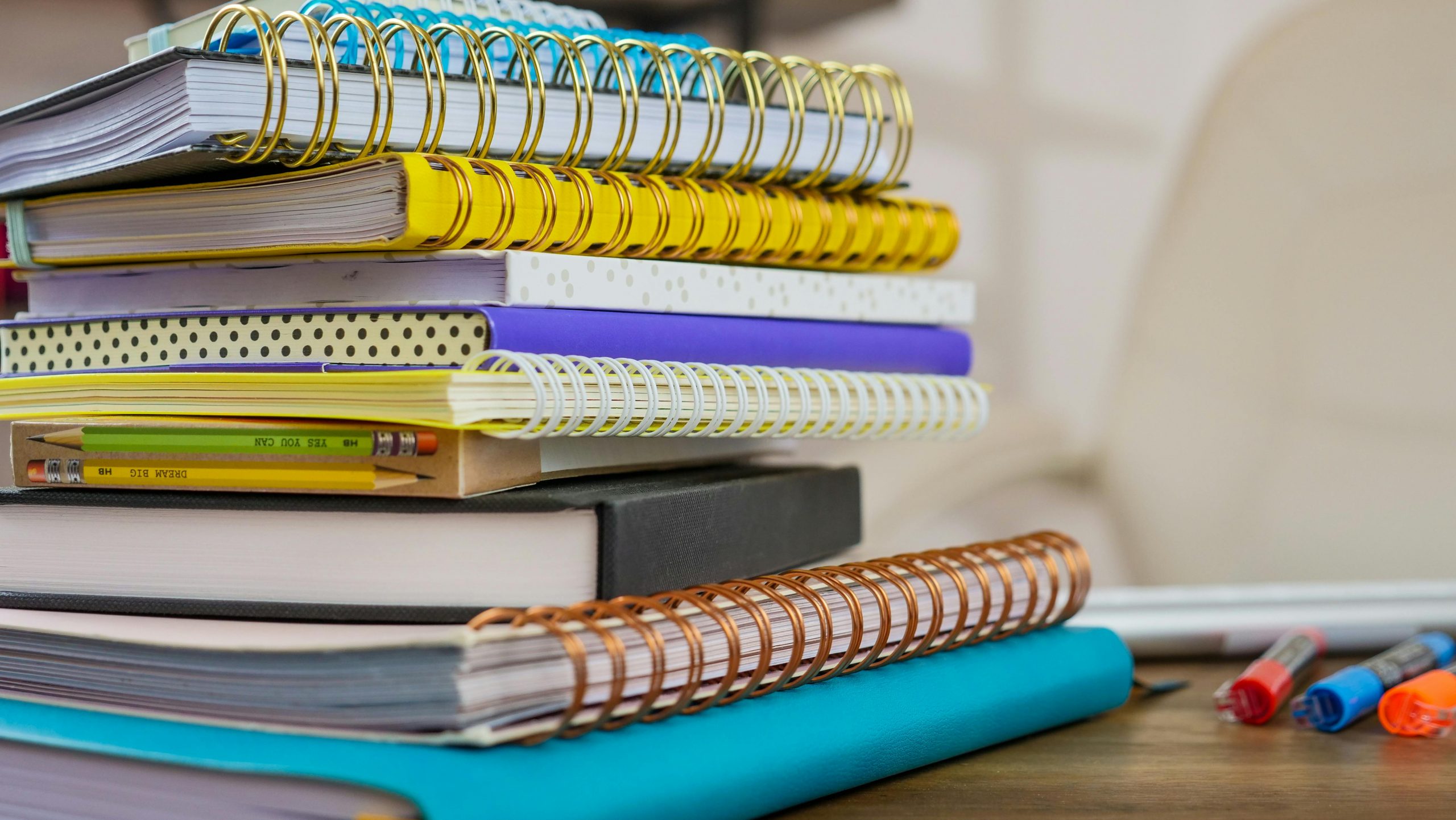 A stack of colorful spiral notebooks and pencils on a wooden desk. Perfect for back-to-school themes.