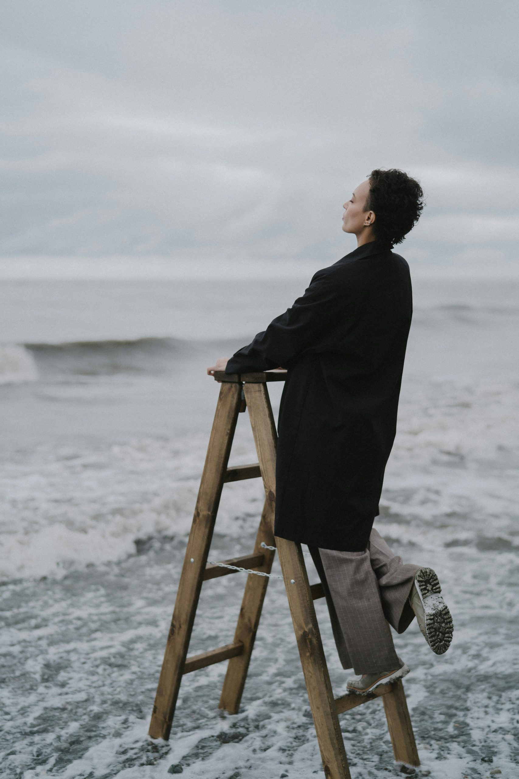 Resources Woman standing on a ladder gazing at the ocean on an overcast day.